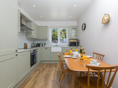 A kitchen with green cabinets a wooden dining table set for breakfast with croissants orange juice and crockery at Verity Mullion