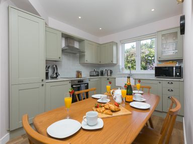 A kitchen with green cabinets wooden dining table set with croissants orange juice and white dishware at Verity in Mullion