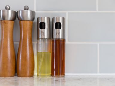 Two wooden pepper mills and two glass oil spray bottles on a kitchen counter against a tiled wall at Verity in Mullion
