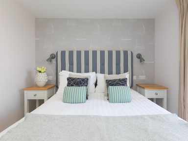 A bedroom with a bed with striped headboard and cushions two bedside tables with lamps and a vase with flowers at Verity Mullion