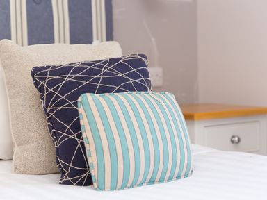 Three pillows stacked on a bed next to a white cabinet with a wooden top at Verity in Mullion
