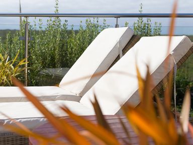 Two white cushioned lounge chairs on a balcony with glass railing and greenery in the background at Verity Mullion