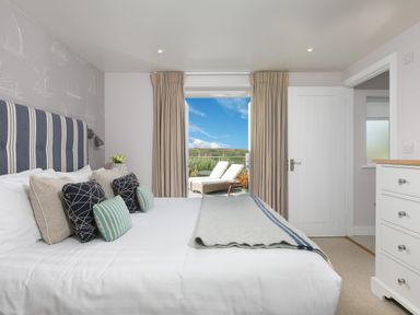 A bedroom with a large bed and pillows and a door opening to an outdoor area with lounge chairs at Verity in Mullion