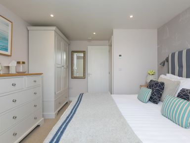 A bedroom with a bed with pillows and a blanket a dresser wardrobe mirror and a door at Verity in Mullion