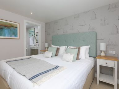A bedroom with a bed and bedside tables with lamps and a bathroom in the background at Verity in Mullion