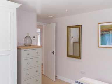 A bedroom with a chest of drawers a wall mirror an open door and framed artwork at Verity in Mullion