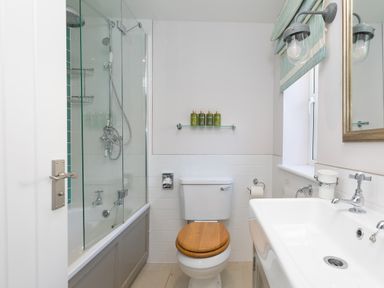 A bathroom with a bathtub and glass shower screen a toilet with a wooden seat a sink with a faucet and mirror and toiletries on a glass shelf at Verity Mullion