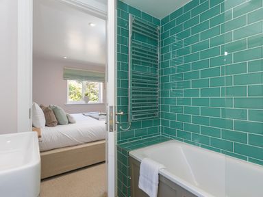 A bathroom with green tiled walls a bathtub and a view into a bedroom with a bed and window at Verity in Mullion