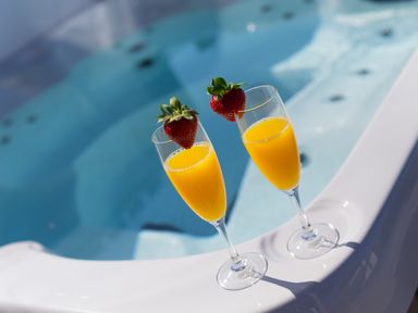 Two glasses of orange juice with strawberries on the rim next to a jacuzzi at Verity in Mullion