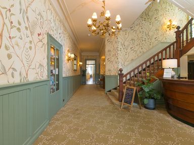 A hallway with floral wallpaper wooden staircase and chandelier at Verity in Mullion