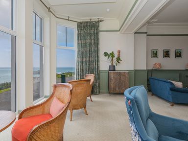 A seating area with wooden chairs and blue armchairs near large windows overlooking the sea at Verity in Mullion