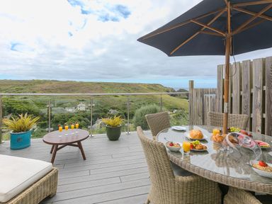 An outdoor patio with a wicker dining set and umbrella overlooking green hills at Daphne in Mullion