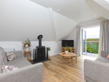 A living room with two grey sofas a small wood stove and a round wood coffee table at Daphne in Mullion