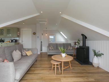An attic living room with two gray sofas a round wooden coffee table a wood stove and plants at Daphne in Mullion
