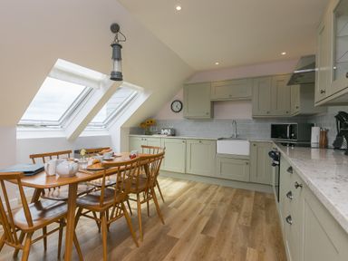 A kitchen with wooden dining table and chairs under skylight windows at Daphne in Mullion