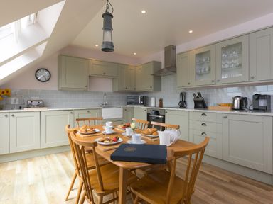 A kitchen with light green cabinets a wooden dining table set for breakfast and skylight windows at Daphne in Mullion