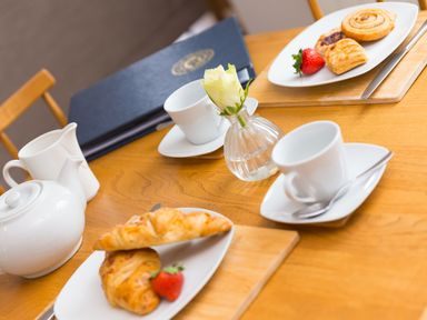 A table set with white teapot and cups plates with pastries and strawberries and a small vase with a white rose at Daphne in Mullion