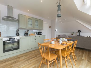 A kitchen and dining area with wooden table and chairs and grey cabinets at Daphne in Mullion