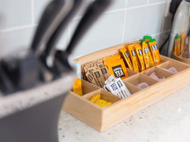 A wooden organizer with tea bags coffee sachets and sugar packets on a kitchen counter at Daphne in Mullion