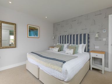 A bedroom with a double bed striped headboard two bedside tables and a wall mirror at Daphne in Mullion