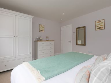 A bedroom with a bed covered by a green throw and pillows a white wardrobe and chest of drawers on walls with fish pictures and a mirror at Daphne in Mullion