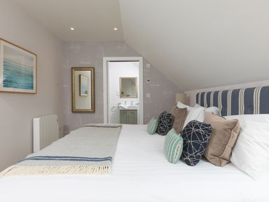 A bedroom with a bed and cushions and a door leading to a bathroom at Daphne in Mullion