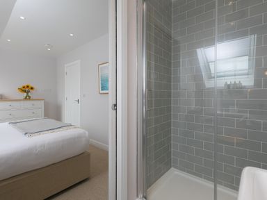 A bedroom with a bed a chest of drawers and flowers next to a shower with grey tile walls at Daphne in Mullion
