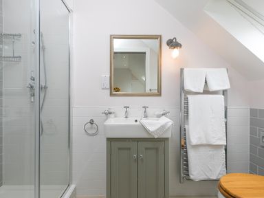 A bathroom with a shower cubicle a sink with mirror above and towels on a towel rack at Daphne Mullion