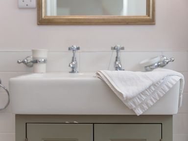 A bathroom sink with chrome taps a white towel on the edge and a holder for a cup at Daphne in Mullion