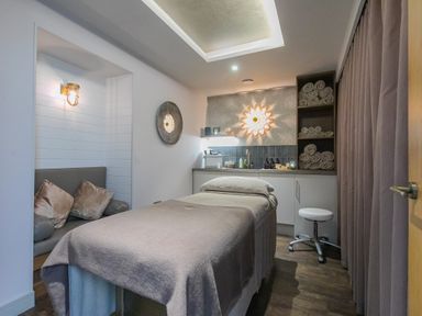 A massage room with a massage table rolled towels and a small seating area at Daphne in Mullion