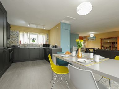 A kitchen with dark cabinets and a dining table with colorful chairs and yellow flowers at 37 Tamar St Ann's Chapel near Callington