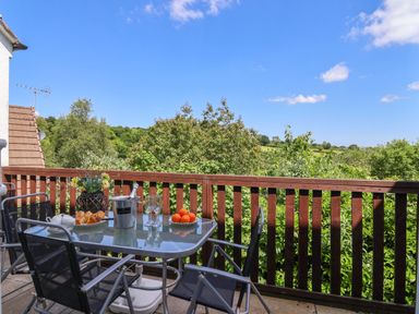 A balcony with a glass table and four chairs overlooking trees and fields at 37 Tamar St Anns Chapel near Callington