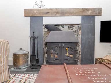 A fireplace with a metal wood stove and fireplace tools on the side at Hole Farm Stables in Bickington near Ashburton