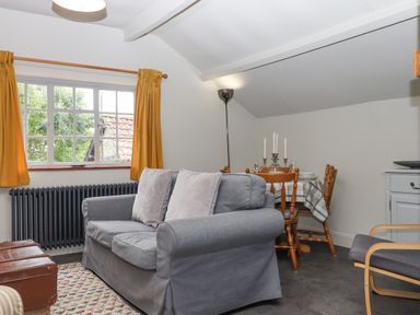 A living room with a grey sofa and two cushions a wooden dining table with chairs and a candelabra by a window with yellow curtains at Hole Farm Stables in Bickington near Ashburton