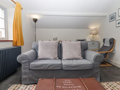 A living room with a grey sofa and cushions a floor lamp and a chair next to a cabinet with a table lamp at Hole Farm Stables in Bickington near Ashburton