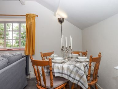A dining area with a round table set with bowls and glasses and wooden chairs near a window with yellow curtains at Hole Farm Stables Bickington near Ashburton