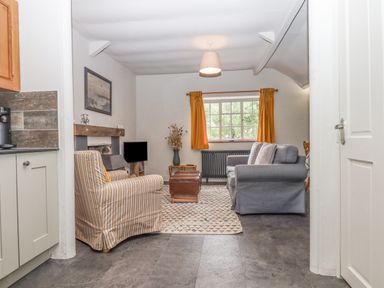 A living room with a striped armchair a grey sofa a window with orange curtains and a rug on the floor at Hole Farm Stables Bickington near Ashburton