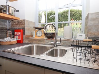 A kitchen sink with a drying rack next to a window with various kitchen items on the windowsill at Hole Farm Stables in Bickington near Ashburton