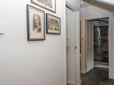A hallway with framed pictures on the wall leading to a bathroom with a glass shower at Hole Farm Stables in Bickington near Ashburton