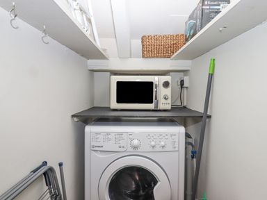 A laundry area with a washing machine and a microwave on a shelf above at Hole Farm Stables in Bickington near Ashburton