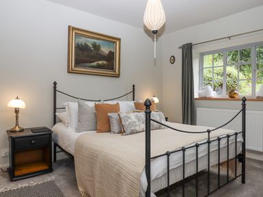 A bedroom with a black metal bed frame side tables lamps and a window at Hole Farm Stables in Bickington near Ashburton