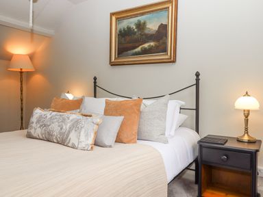 A bedroom with a bed featuring several pillows a bedside table with a lamp and a painting on the wall at Hole Farm Stables in Bickington near Ashburton