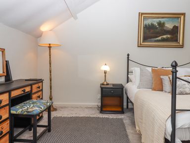 A bedroom with a bed and pillows a nightstand with a lamp a dresser with a mirror a stool and a floor lamp at Hole Farm Stables in Bickington near Ashburton