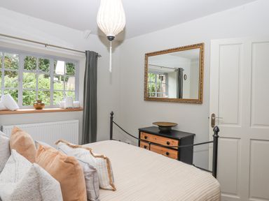 A bedroom with a bed with multiple pillows a window with rolled towels a black and wood dresser and a wall mirror at Hole Farm Stables in Bickington near Ashburton