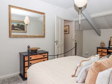 A bedroom with a bed with pillows a black and wooden dresser a large mirror and a doorway at Hole Farm Stables in Bickington near Ashburton
