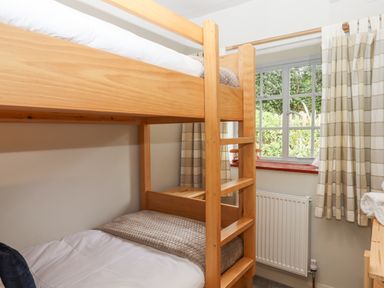 A bedroom with wooden bunk beds next to a window with checked curtains at Hole Farm Stables in Bickington near Ashburton