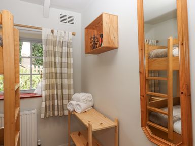 A small room with wooden bunk beds a wooden shelf with rolled towels a window with checkered curtains and a wall mirror at Hole Farm Stables in Bickington near Ashburton