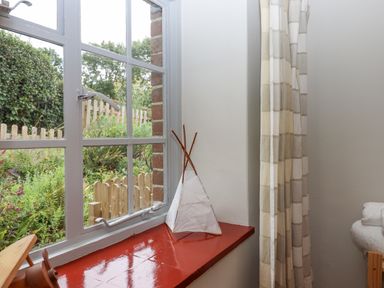 A window with a red windowsill white curtains and a small white decorative teepee on the sill at Hole Farm Stables in Bickington near Ashburton