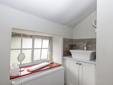 A bathroom sink and cabinet with a window ledge holding a rolled towel tissue paper and a small mirror at Hole Farm Stables Bickington near Ashburton