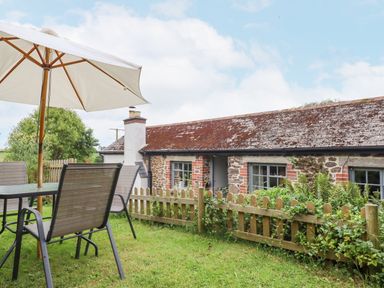 A garden with outdoor table and chairs under umbrella next to a stone cottage at Hole Farm Stables in Bickington near Ashburton